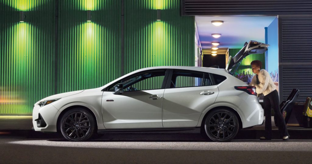 The 2025 Subaru Impreza in white parked on a city street at night.