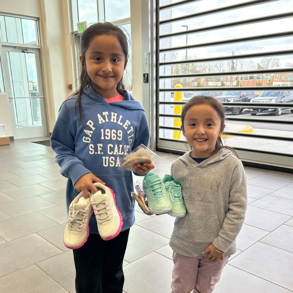 Two little girls each hold a pair of shoes that were donated at Wyatt Johnson Subaru's shoe and sock drive in Clarksville, TN.