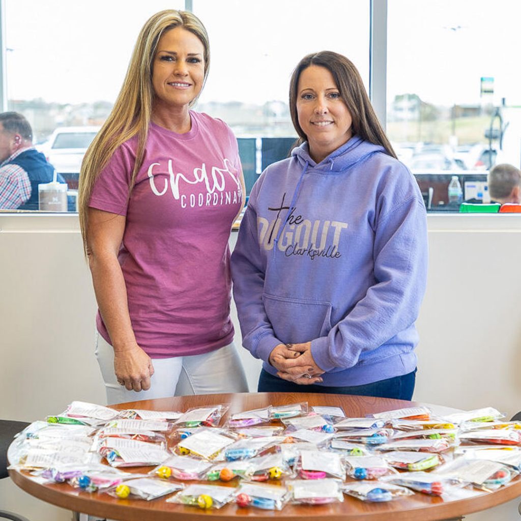 Two women pose for a picture with goody bags on a table in front of them as they participate and help in Wyatt Johnson Subaru's shoe drive in Clarksville, TN.
